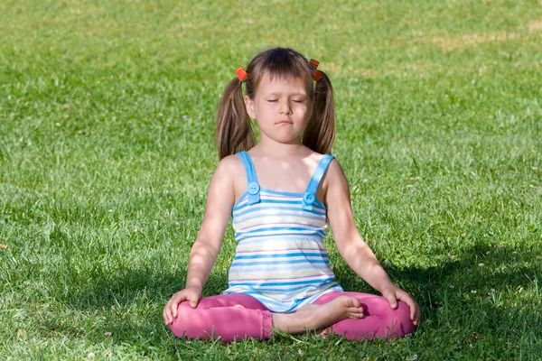 Criança pequena sentar e meditar em asana na grama verde — Fotografia de Stock