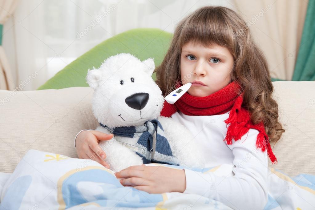 Little sick girl with thermometer embraces toy bear in bed
