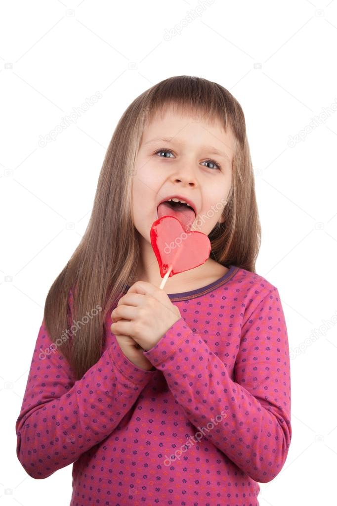 Little girl 7-8 years old licking red heart lollipop isolated