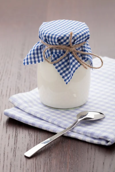 Hausgemachter Milchjoghurt im Glastopf und Löffel auf dem Tisch Stockfoto