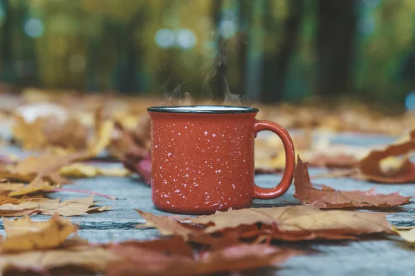 Autumn coffee or tea in a cup on a wooden table against the background of yellow fallen leaves and October weather. Autumn drink, mood and comfort concept.