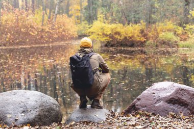 Ormanda bir gezgin. Sırt çantalı bir adam güzel bir sonbahar ormanında yolda yürüyor ve takılıp düşüyor ve göle ve doğal manzaraya hayran kalıyor. Ormanda yalnız başına doğaya seyahat etmek.