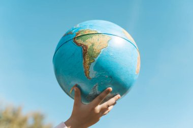 Temiz bir arka planda bir küreyle el. Güneşli yaz havasında dünya gezegeniyle el ele tutuşan çocuklar. Çevre koruma, ekoloji, doğa kavramı.