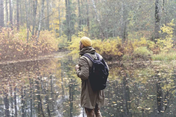 Reiziger in het bos. Een man met een rugzak wandelt en struikelt over een baan in een prachtig herfstbos en bewondert het meer en het natuurlijke uitzicht. Reizen naar de natuur in het bos alleen — Stockfoto