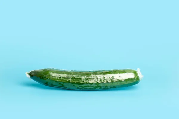 Vegetables in plastic packaging from the supermarket are minimal. Cucumber in cellophane and non-degradable plastic on a blue background. Biodegradable product packaging, environmental protection