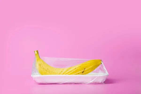 Frutas em embalagens plásticas do supermercado são mínimas. Banana em celofane e plástico não degradável sobre fundo azul. Embalagem de produtos biodegradáveis, protecção do ambiente, natureza — Fotografia de Stock
