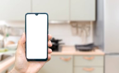 Mutfak arka planında telefonla el işi. Boş akıllı telefon ekranlı bulanık bir ev mutfağı. Çevrimiçi market siparişi konsepti, çevrimiçi gıda alışverişi. Yüksek kalite fotoğraf