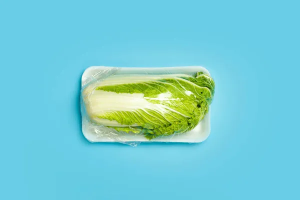 Warzywa w plastikowych opakowaniach z supermarketu są minimalne. Kapusta chińska w celofanie i niezniszczalny plastik na niebieskim tle. Opakowania produktów ulegających biodegradacji, ekologiczne — Zdjęcie stockowe