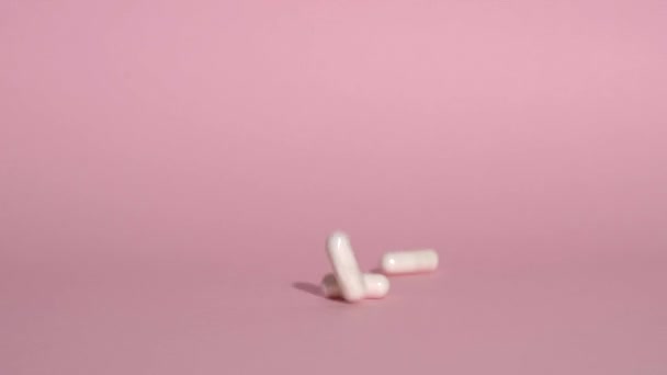 Pastillas cayendo sobre un fondo rosa. Las tabletas de medicina blanca o vitaminas se vierten lentamente. Farmacología, productos farmacéuticos, suplementos, tratamiento y concepto de salud. — Vídeos de Stock