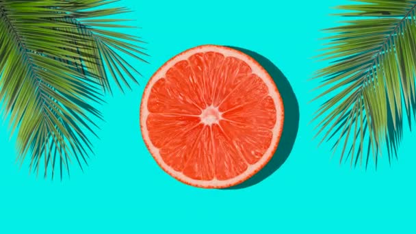 Orange rotieren im Sonnenlicht mit Palmenschatten auf einem farbigen blauen Hintergrund. Fruchtsäfte, Entspannung, Tropen und Entspannungskonzept. — Stockvideo