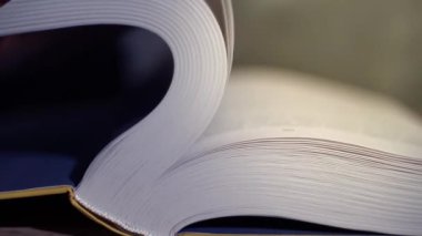 Kitabın yakın çekim sayfaları kütüphanedeki masanın üzerinde çevriliyor. Okuma, çalışma, edebiyat, bilgi kavramı.