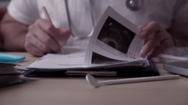 Masadaki klinikte çalışan bir doktor. Doktor hastanın ultrason görüntüsünü inceliyor, teşhis koyuyor, bir sonuç çıkarıyor ve tedavi öneriyor..