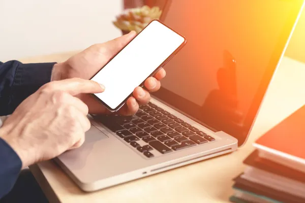 Phone and laptop in hand on the desktop in the office or at home. Smartphone blank screen mockup. Using web, shop, apps concept. — Stock Photo, Image