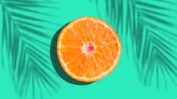 Апельсин вращается в солнечном свете с тенями ладони на цветном голубом фоне. Фруктовые соки, релаксация, тропики и релаксация. — стоковое видео