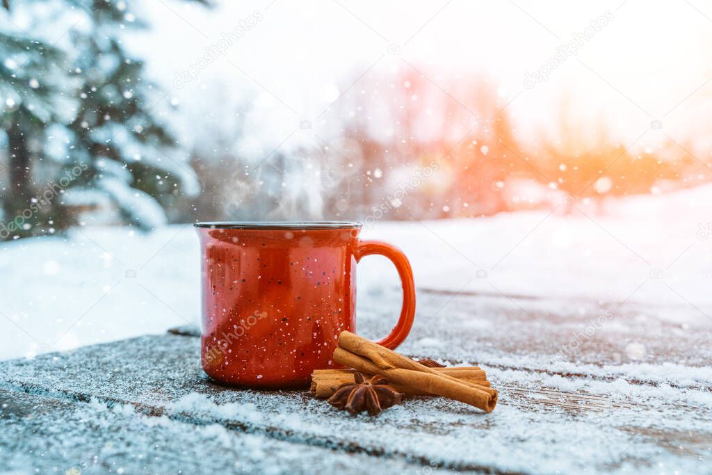 Mulled wine or tea on a wooden background during a snowfall in the forest. Winter hot drinks with aromatic spices of cinnamon, cardamom and orange. Warmth, comfort and atmosphere of December nature