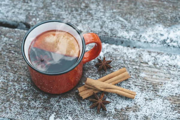 Anggur atau teh di latar belakang kayu saat salju turun di hutan. Minuman panas musim dingin dengan rempah-rempah dari kayu manis, kapulaga dan oranye. Kehangatan, kenyamanan dan suasana Desember alam — Stok Foto