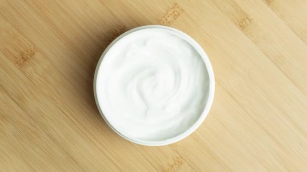 Cosmetische crème achtergrond. Witte cosmetische crème in pot voor huid- en lichaamsverzorging met textuur roteert op houten bamboe ondergrond — Stockvideo