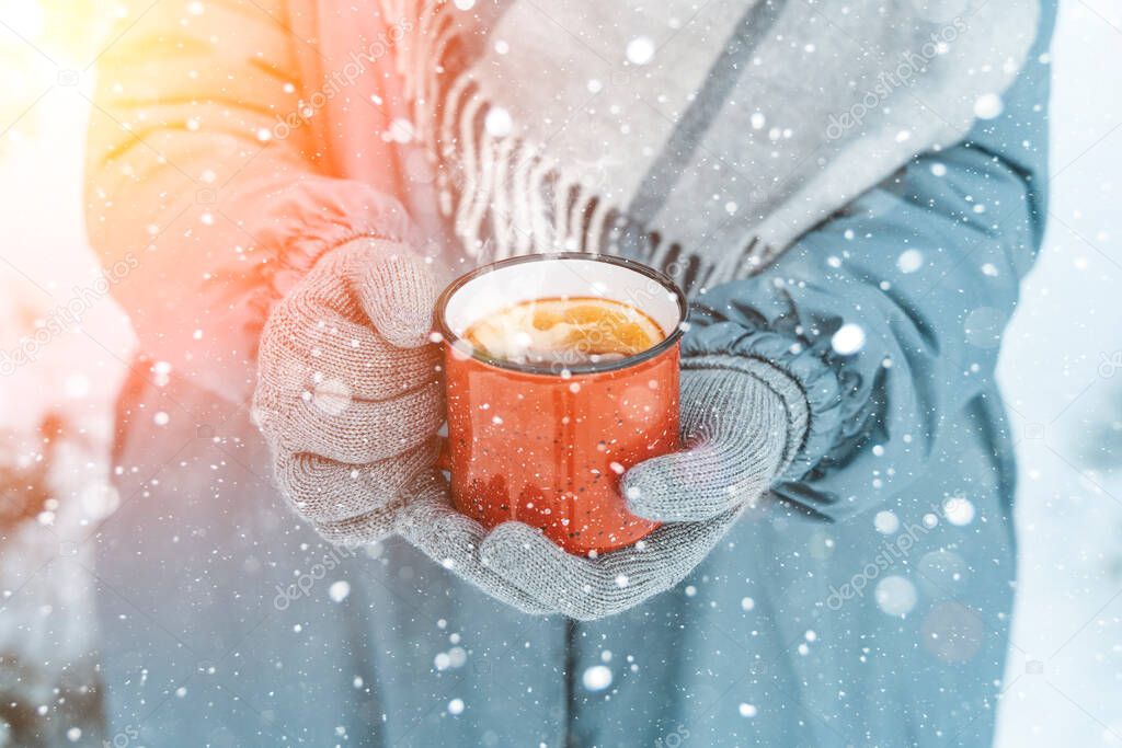 Mulled wine in the hands of a girl during a snowfall in the forest. Winter hot drinks with aromatic spices of cinnamon, cardamom and orange. Warmth, comfort and atmosphere of December nature and
