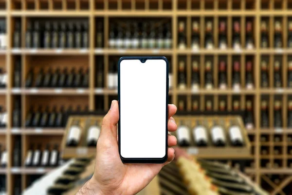Wine shop with bottles background. Hand with blank smartphone screen one wine backdrop. Buying and ordering alcoholic beverages online — Stock Photo, Image
