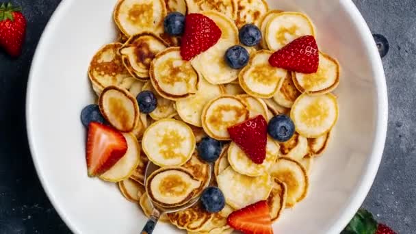 ボウルにパンケーキシリアル朝食を回転させます.健康的な食事のためのキッチンテーブルの上に新鮮なベリーとミニパンケーキ. — ストック動画