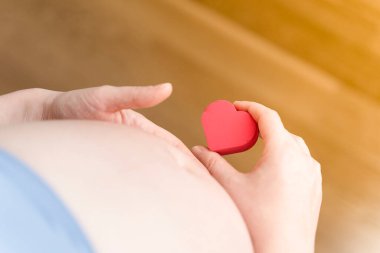 Tüp bebek taktıktan sonra hamile bir kadın elinde küçük kırmızı bir kalp tutuyor. Tüp bebek, annelik, doğurganlık, yeni hayat kavramı..