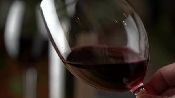 Um copo de vinho tinto. Degustação de vinhos derramando em um copo no fundo de uma mesa de madeira de um restaurante ou bar. Sabor, aroma, riqueza. Bebidas alcoólicas do conceito de vindima. — Vídeo de Stock