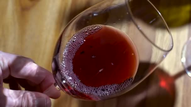 Um copo de vinho tinto. Degustação de vinhos derramando em um copo no fundo de uma mesa de madeira de um restaurante ou bar. Sabor, aroma, riqueza. Bebidas alcoólicas do conceito de vindima. — Vídeo de Stock