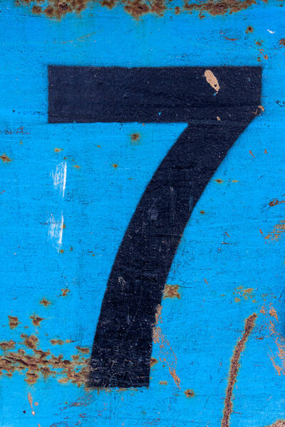 Number 7 in black paint on an old blue iron surface with rust texture and traces of dirt.