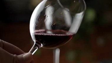 Bir kadeh kırmızı şarap. Şarap tatma bir restoranın ya da barın ahşap masasının arka planında bir bardağa dökülüyor. Tat, aroma, zenginlik. Üzüm hasadı konseptinden alkollü içecekler.