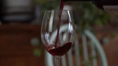 Bir kadeh kırmızı şarap. Şarap tatma bir restoranın ya da barın ahşap masasının arka planında bir bardağa dökülüyor. Tat, aroma, zenginlik. Üzüm hasadı konseptinden alkollü içecekler.