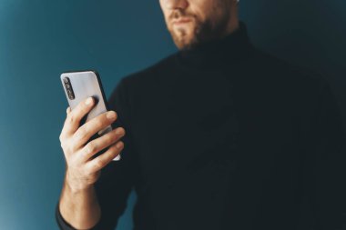 Boş bir arkaplanda genç bir adamın akıllı telefonunu kullanmak. İnternet 'i, kuryeyi, alışverişi, iletişimi kullanırken telefon elinde. Teknoloji, uygulamalar, iş konsepti.