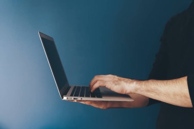 Karanlık duvar arka planında dizüstü bilgisayarı olan bir adam. Eğitim, iş, teknoloji kavramı.