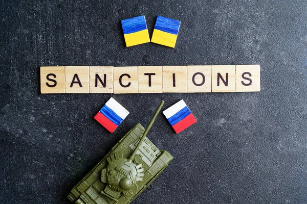Sanções contra o conceito da Rússia. Tanque de brinquedo e a inscrição Sanções em um fundo escuro. Conflito de guerra na Ucrânia, incumprimento, crise económica e monetária na Rússia. — Fotografia de Stock