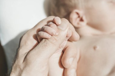 Bebek eli. Baba şefkatle kucaklıyor ve yeni doğan bebeğin küçük elini seviyor. Yeni hayat, ebeveyn koruması, bakım, aşk, çocuk ve bebek sağlığı