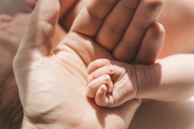 Bebek eli. Baba şefkatle kucaklıyor ve yeni doğan bebeğin küçük elini seviyor. Yeni hayat, ebeveyn koruması, bakım, aşk, çocuk ve bebek sağlığı