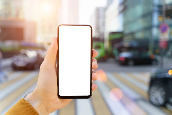 A smartphone in a hand with a blank screen against the backdrop of an urban street of the business quarter of the city. Business applications, transport, taxi, maps concept — Stock Photo, Image