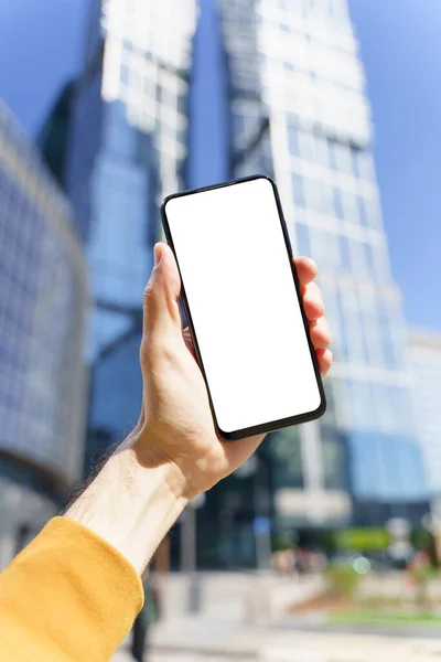 Elinde boş bir ekranla bir akıllı telefon şehrin iş merkezindeki bir sokak arkaplanının önünde. İş başvuruları, ulaşım, taksi, harita kavramı — Stok fotoğraf