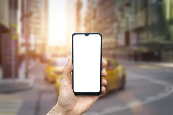 A smartphone in a hand with a blank screen against the backdrop of an urban street of the business quarter of the city. Business applications, transport, taxi, maps concept — Stock Photo, Image