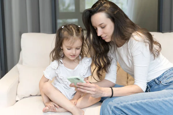 Mom and daughter use smartphone while playing and learning. Technology, internet and children. Parenthood, education, training, free time with children concept. High quality photo