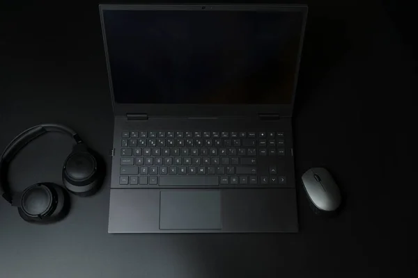 Headphones and laptop computer on black desktop. Listening to music, audio, sound concept. High quality photo