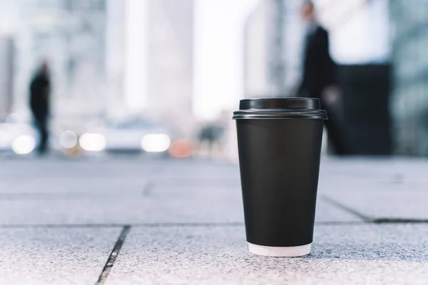 Takeaway coffee in a paper cup. Hot drink to go on the background of a busy city street. Paper cup mockup. High quality photo
