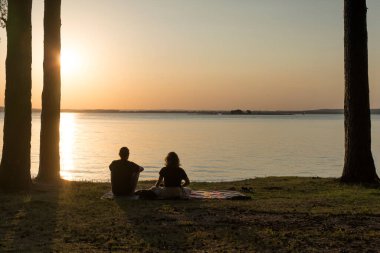 Romantic couple is resting at sunset on the shore of a forest lake. Nature, love, relaxation concept. High quality photo