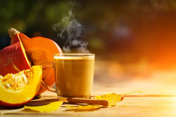 Pumpkin latte coffee with spices and cinnamon. Autumn hot drink on a rustic wooden table decorated with yellow leaves and pumpkin under the sun. Cosiness, halloween, warmth concept. . High quality