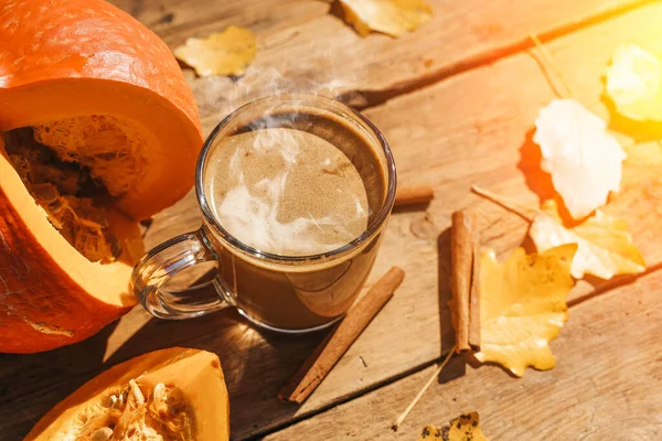 Pumpkin latte coffee with spices and cinnamon. Autumn hot drink on a rustic wooden table decorated with yellow leaves and pumpkin under the sun. Cosiness, halloween, warmth concept. . High quality