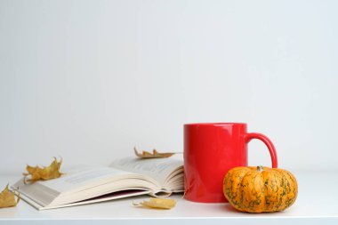 Kitap, fincan ve sonbahar balkabağı. Arka planda yapraklar var. Sonbahar tatilinin atmosferi ve konforu ve havası. Okuma, ev kavramı. Yüksek kalite fotoğraf