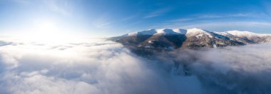 Dağlarda görkemli bir gündoğumu görüntüsü. Dağlar arasındaki vadi sisle kaplıdır ve yükselen güneşin sıcak ışınlarıyla aydınlanır. Dağlar doğal ormanlarla kaplı..