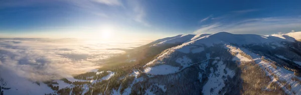 Vue aérienne du lever du soleil majestueux dans les montagnes. La vallée entre les montagnes est couverte de brouillard et est éclairée par les rayons chauds du soleil levant. Montagnes couvertes de forêt naturelle. — Photo