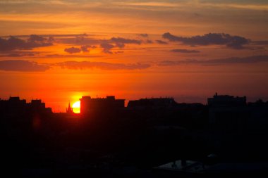Yaz güneşi, şehir binasının arka planına karşı şehrin çatı manzarası ile gün batımının altın saatini bulanıklaştırıyor. Kentsel manzara sıcak sıcak ısı ufku