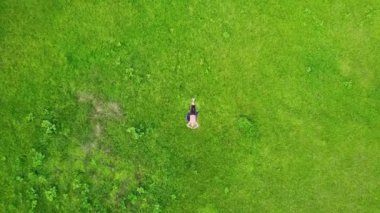 Havadan bakış açısı. Yeşil çimlerin üzerinde uzanan bir kızın etrafında sihirli otlarla kaplı bir düzlükte alçak yörüngede uçmak. Günlük giysi ve zen meditasyon duruşu. Karpatlar, Ukrayna