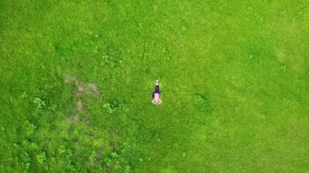 Punto di vista aereo. Volare in orbita bassa intorno a una ragazza sdraiata su erba verde in una meravigliosa radura coperta di erba magica. Indossare ogni giorno e zen meditazione postura. Carpazi, Ucraina — Video Stock